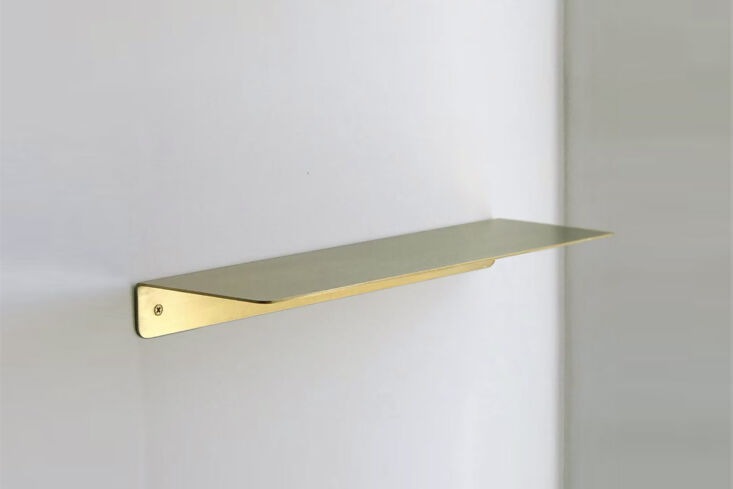 A small solid brass wall shelf displaying decorative items.