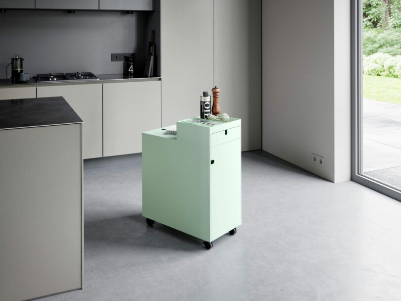 A mint green mobile cart used as a storage unit in a minimalist kitchen setting.