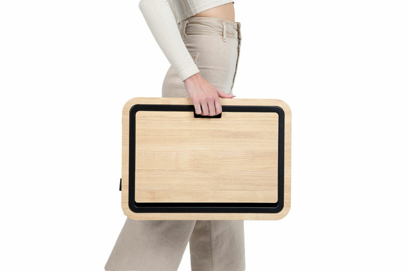 A person holding the Arlo Skye lap desk by its side handle against a white background.