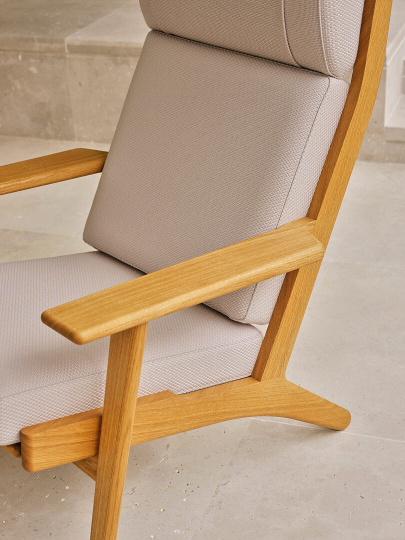 A close-up of the CH290 armchair's wooden armrest and light beige upholstery.