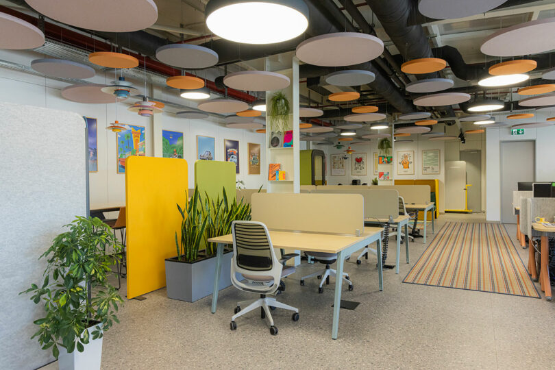 Modern open-plan office interior with white desks and colorful acoustic panels on the ceiling for noise reduction.