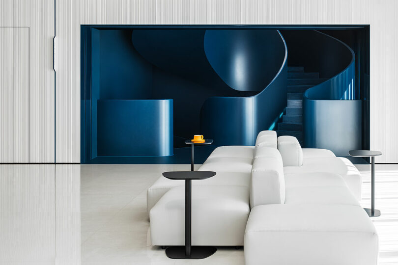 White modular seating in front of a sculptural deep blue spiral staircase.