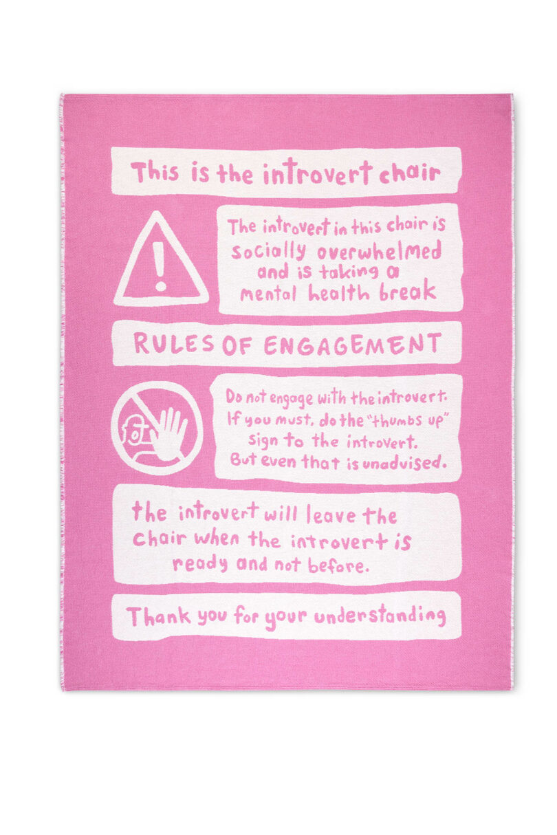 A pink blanket with white text listing the rules of the Introvert Chair, such as 'No questions' and 'Be kind'.