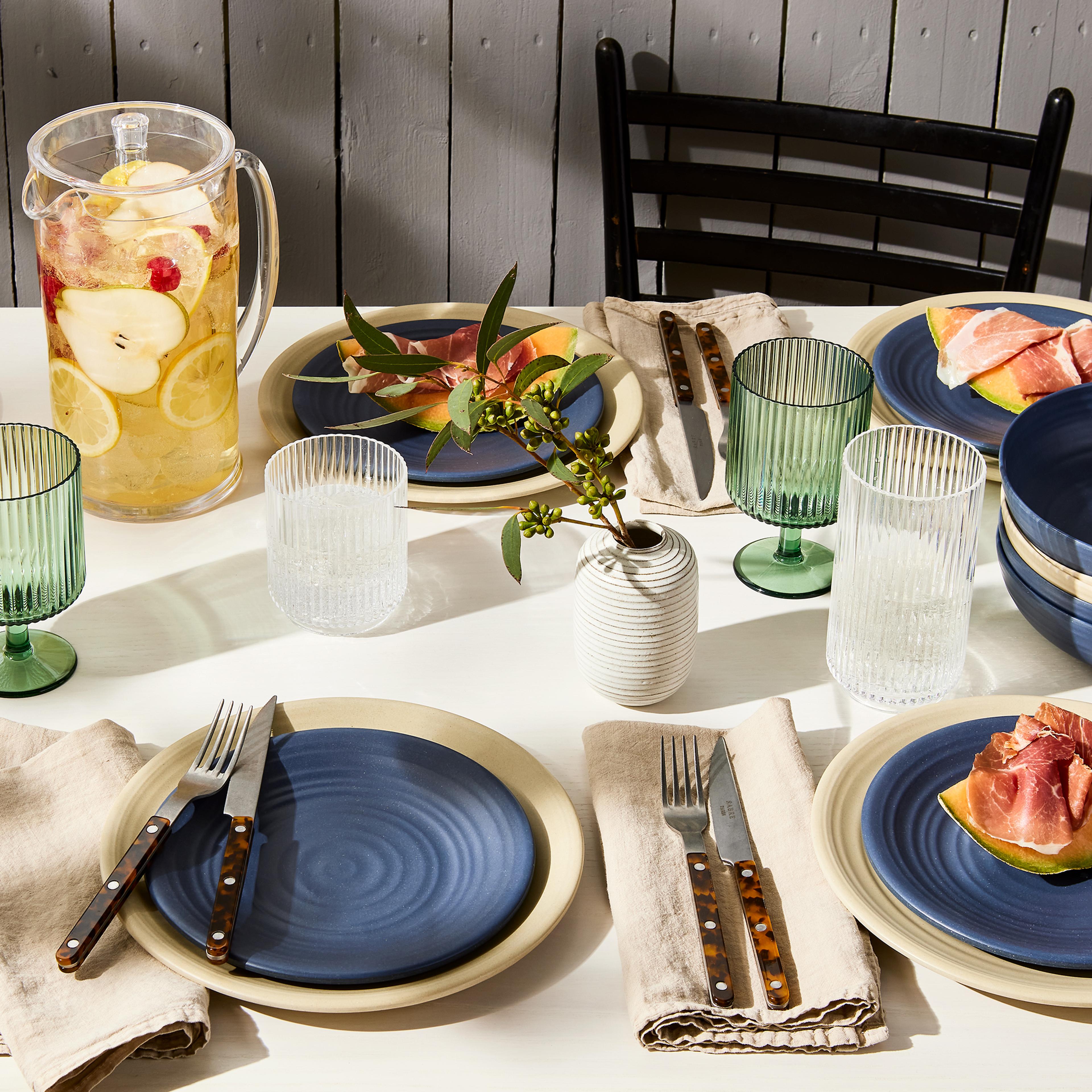 A beautifully set summer table outdoors with dinnerware and organic textures.