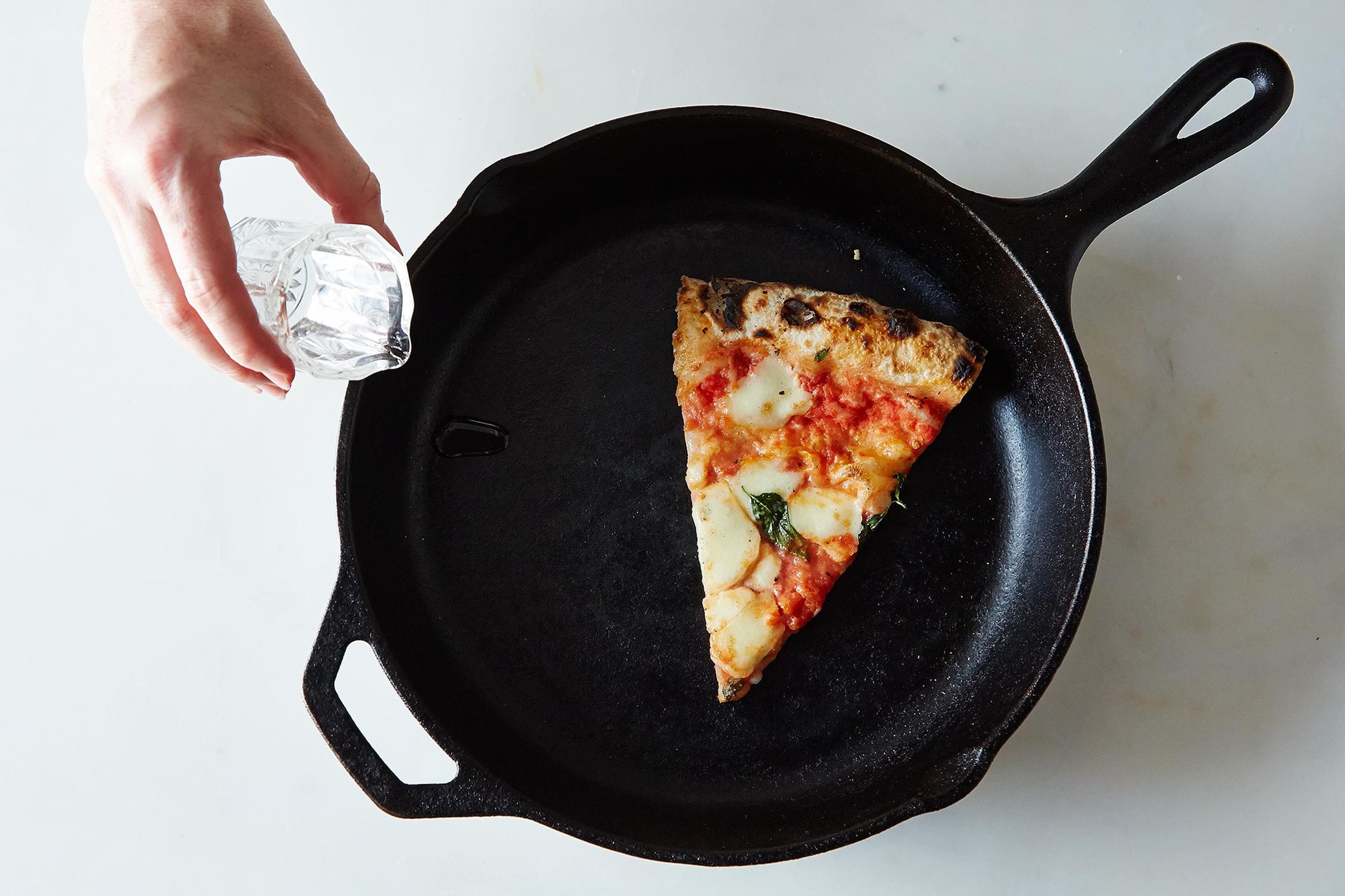 Leftover pizza being reheated to a crisp in a black cast-iron skillet on a stovetop.