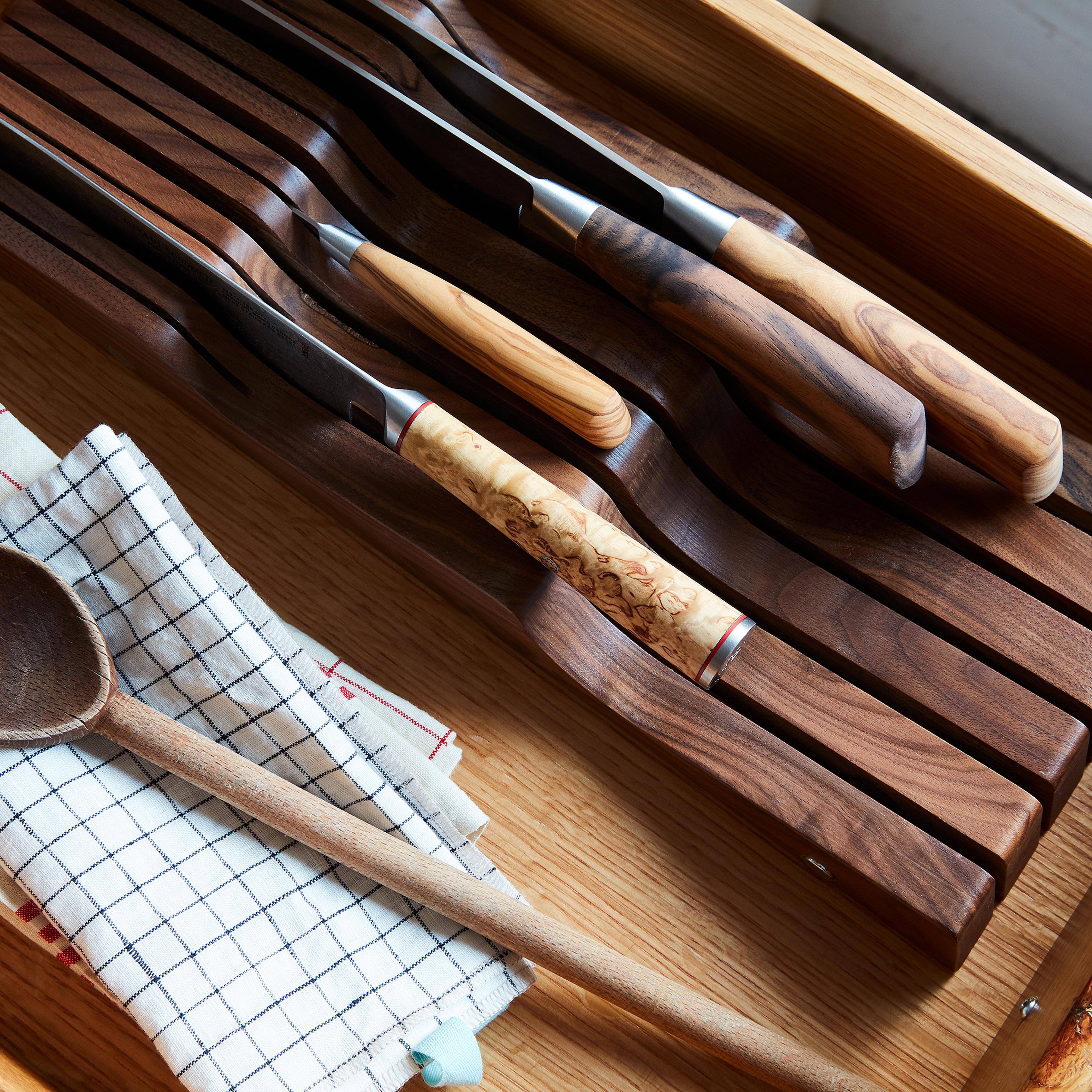 A wooden drawer organizer holding a small set of high-quality kitchen knives.