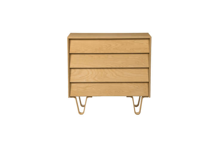 A mid-century modern four-drawer wooden dresser against a wood-paneled wall.