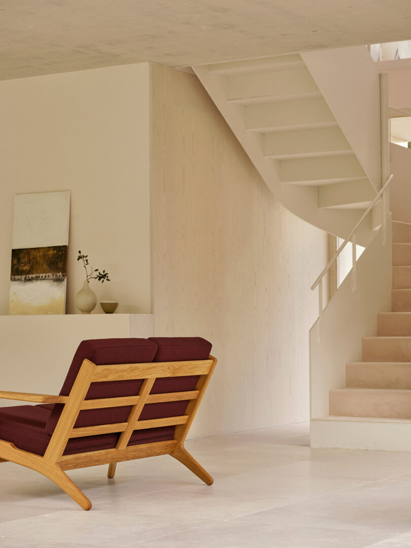 A CH290 lounge chair with burgundy cushions next to a white curved staircase.