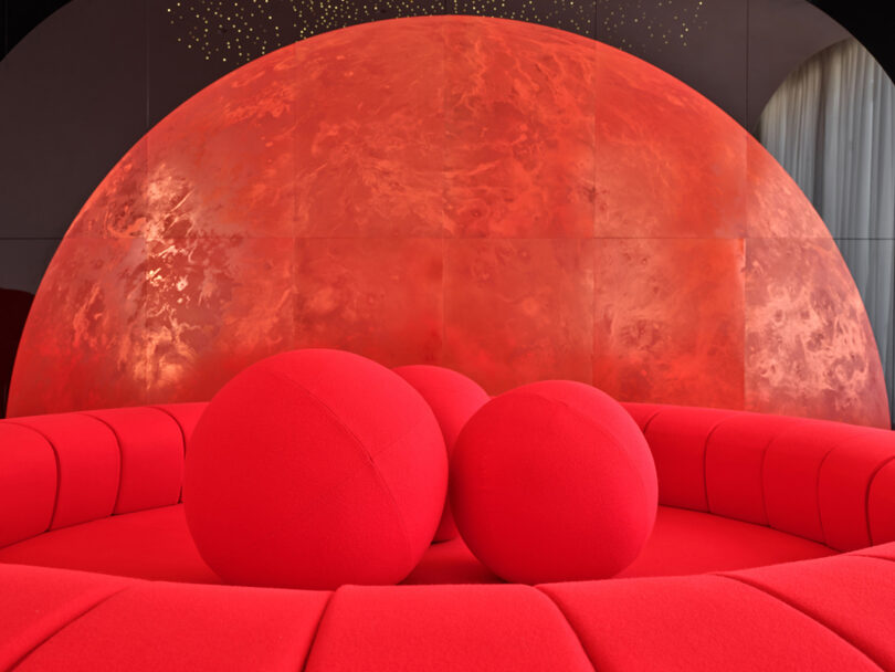 A circular red couch in front of a massive, illuminated red semi-circular backdrop resembling a planet.