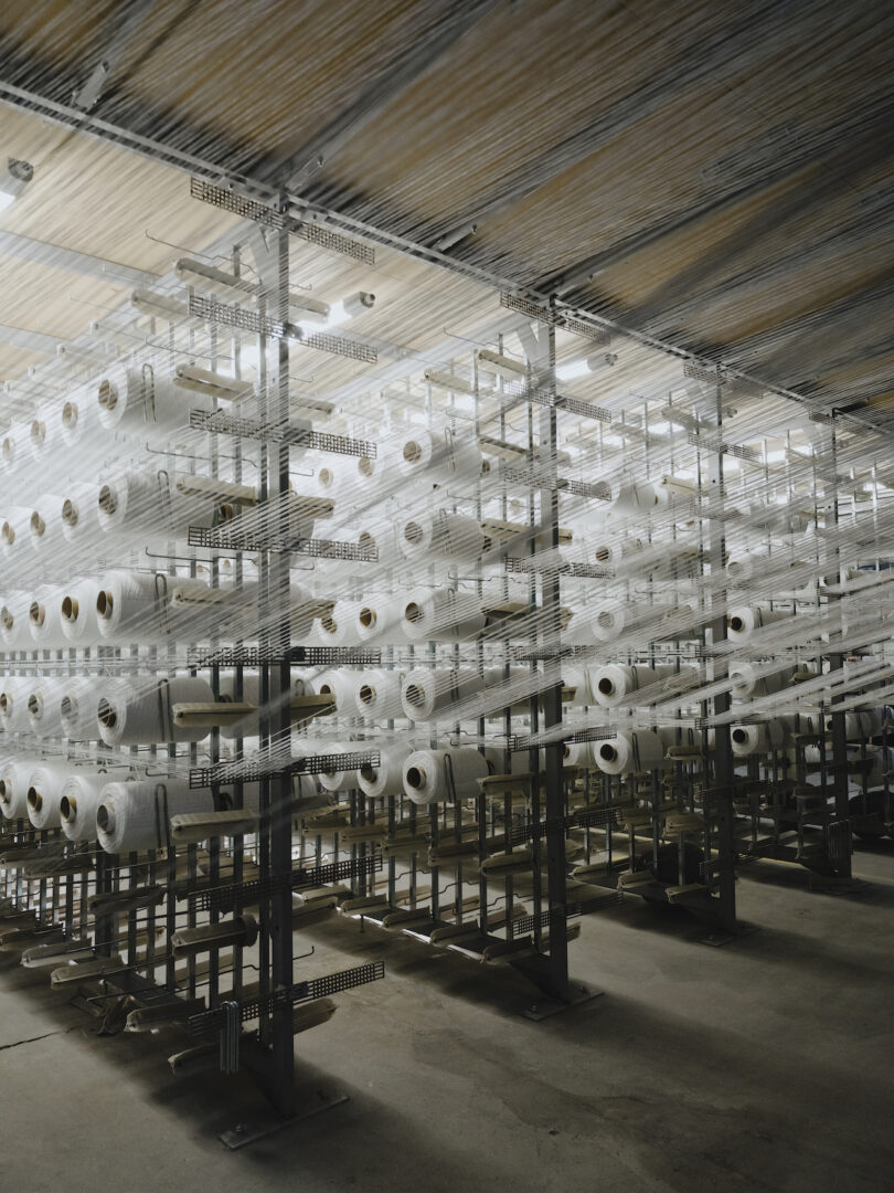 Industrial metal racks holding numerous white spools of thread in a textile factory.