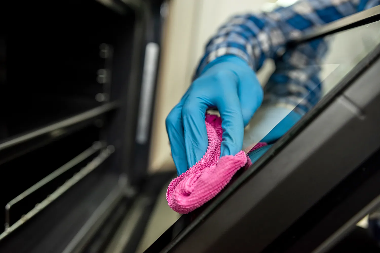 A person cleaning the interior glass of a stainless steel oven door with a microfiber cloth.