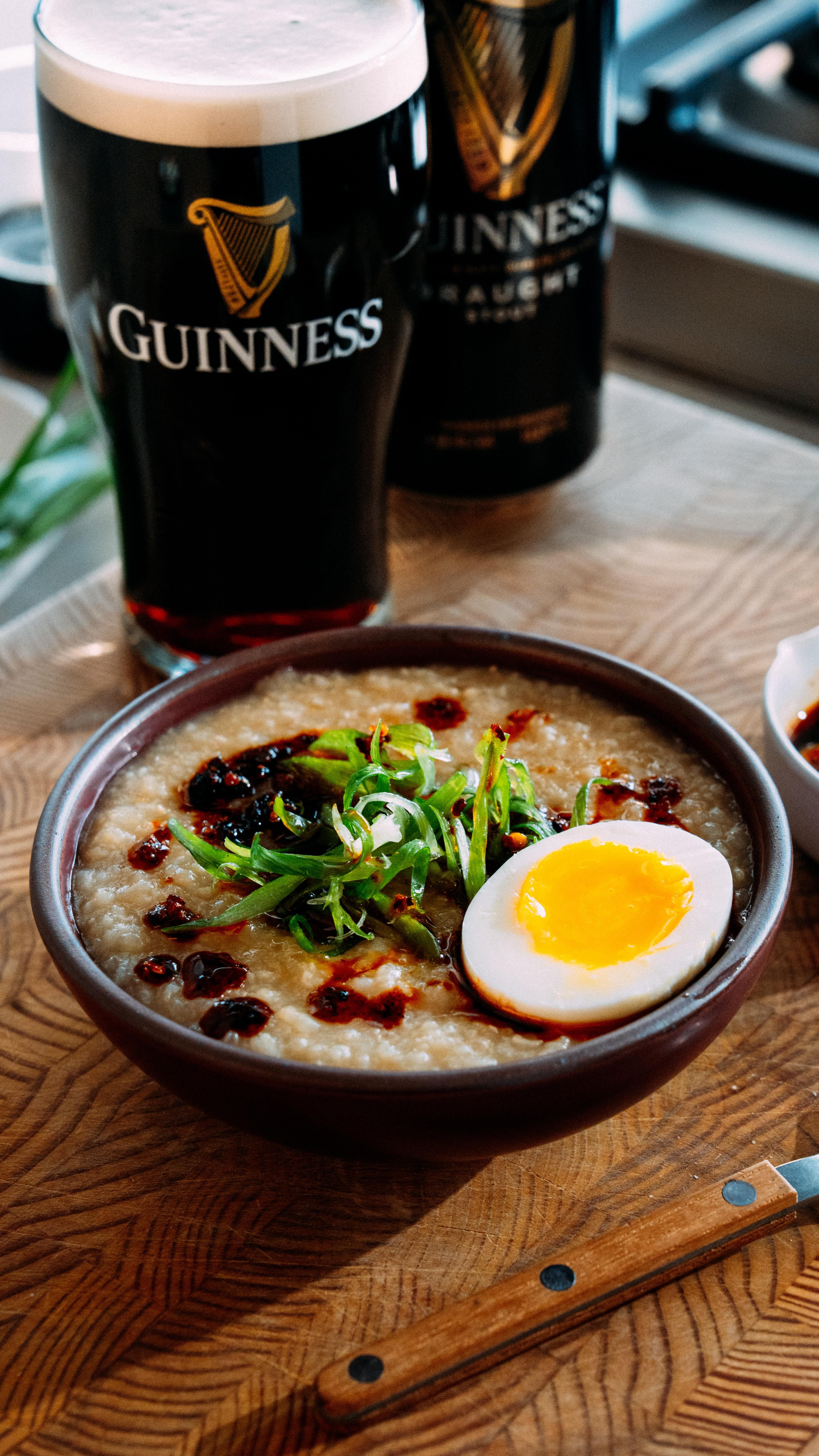 A glass of dark Guinness stout next to a savory bowl of congee.