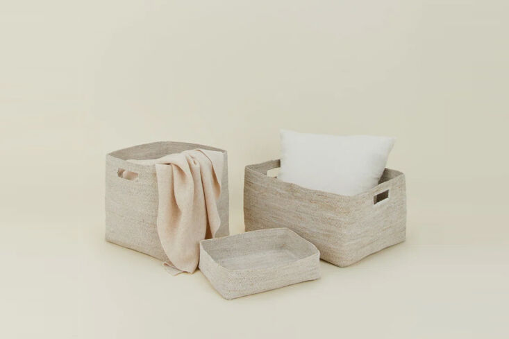 A natural seagrass basket holding a bright yellow knitted throw blanket.