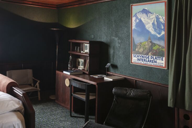 A guest room with dark walnut furniture, a Charlotte Perriand LC4 chaise, and deep forest green walls.