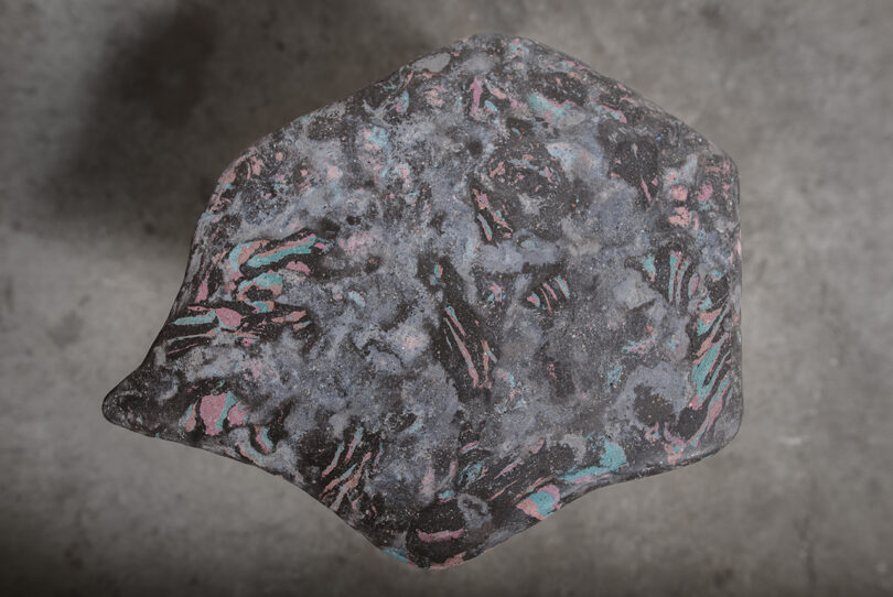 Close-up of Neo-Scagliola material showing pink and turquoise recycled accents in a gray stone-like base.