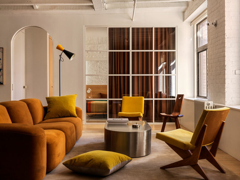 A glass and steel partition separating a living room from a bedroom area with brown curtains.