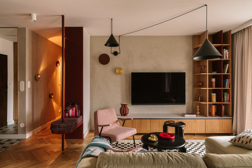 Vibrant living room with a green corduroy sofa, pink armchair, and geometric wall decor.