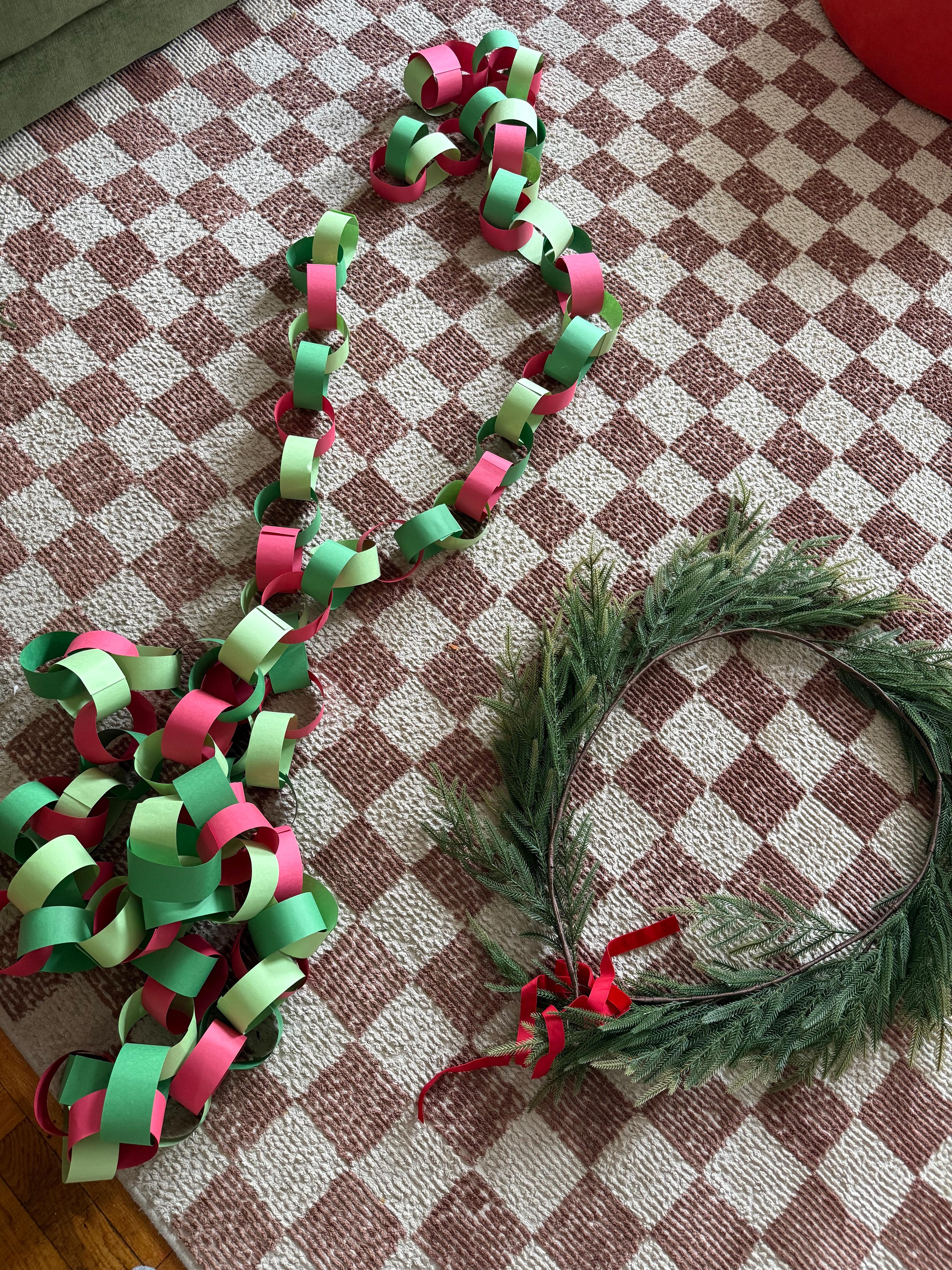 A simple holiday wreath and paper chain decoration against a neutral wall.