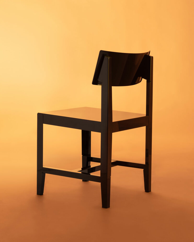 A modern black Bishop chair with a solid backrest positioned against a vibrant orange background.