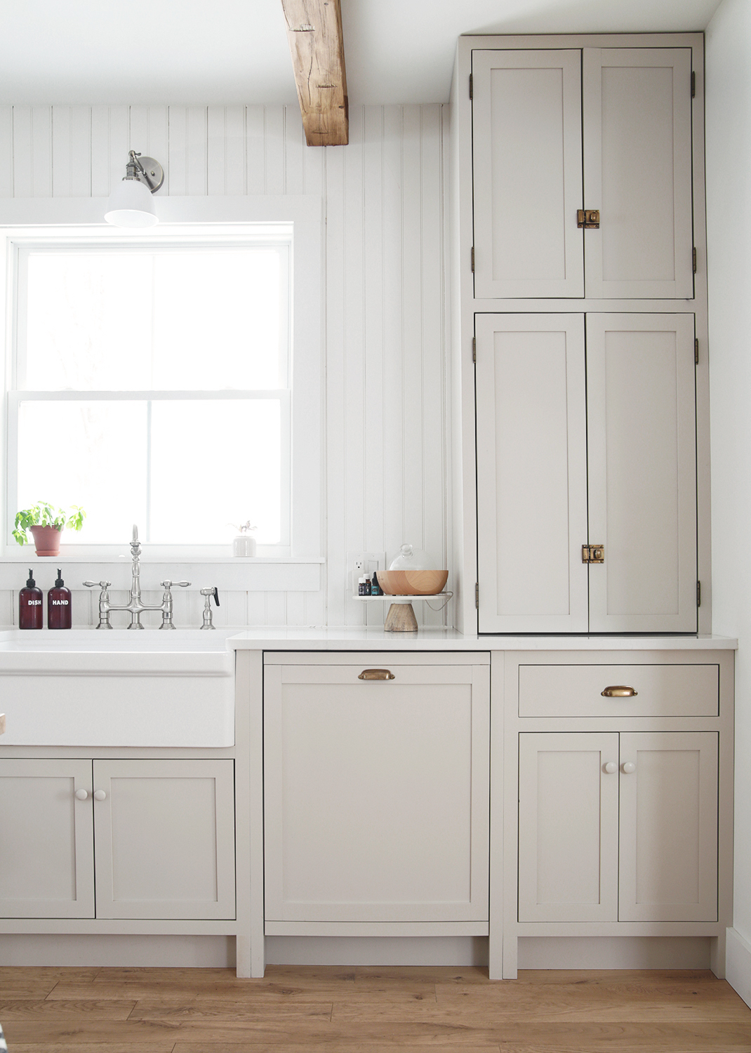 A fully camouflaged dishwasher integrated into green Shaker-style kitchen cabinets with brass hardware.