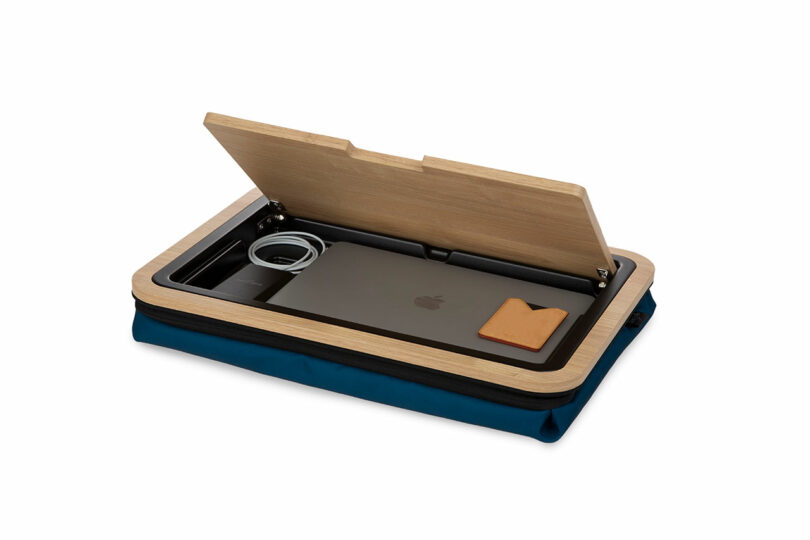 The wooden lid of the lap desk is open to reveal a laptop and charging accessories stored inside.