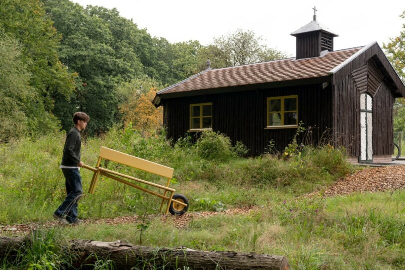 A person pushing the yellow Wheelbench by its handles along a garden path.