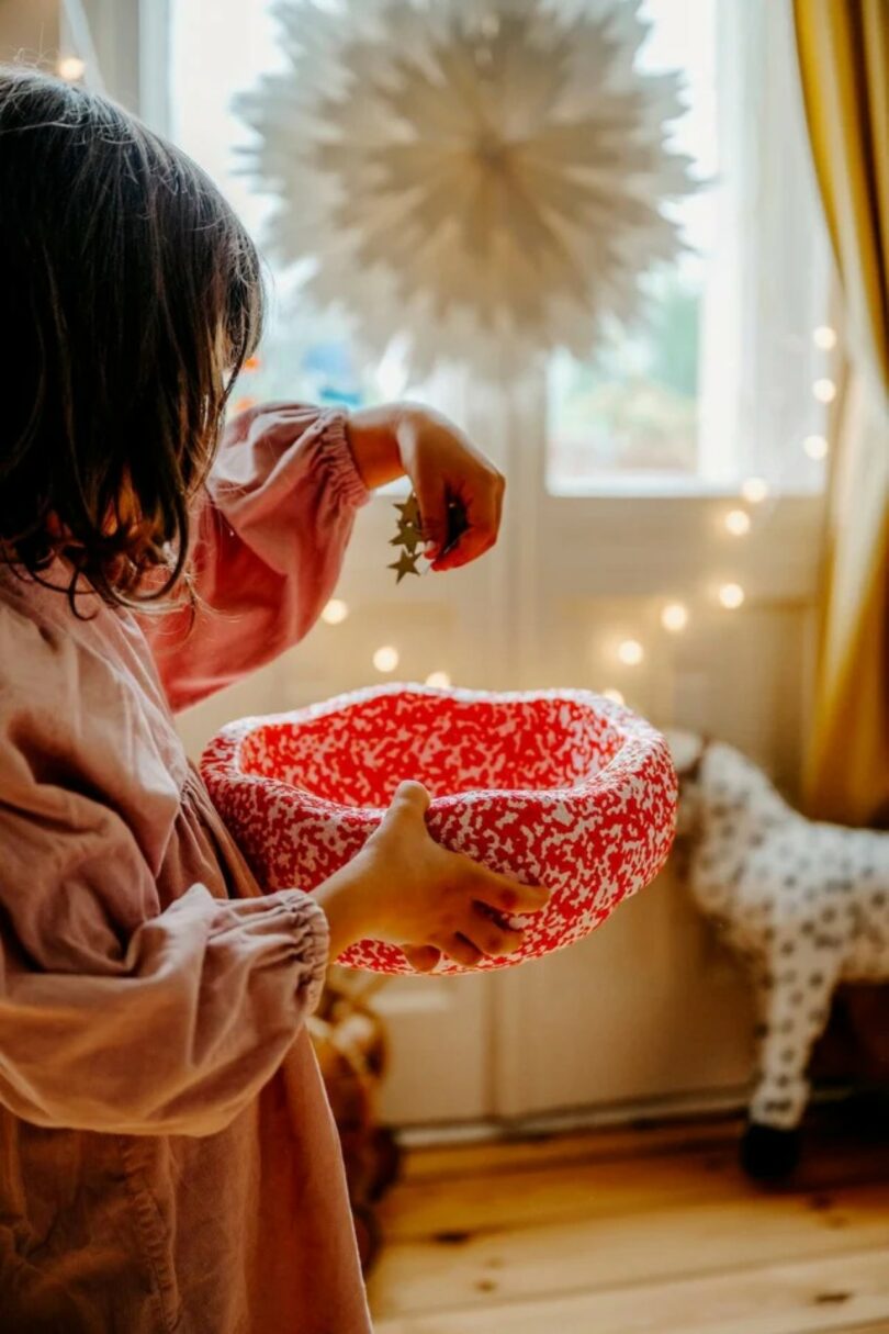 A person in a pink dress holding a red patterned ceramic bowl over a festive table.