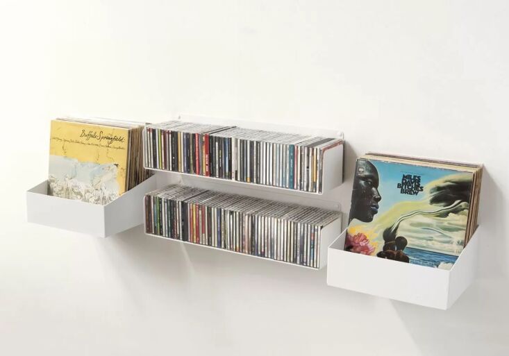 Minimalist white U-shaped floating shelves holding CDs and vinyl records.