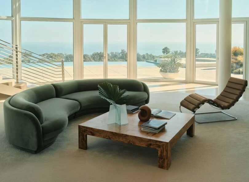 A modern living room featuring the Poet Sofa in Malibu Willow green velvet overlooking a lush garden and pool.