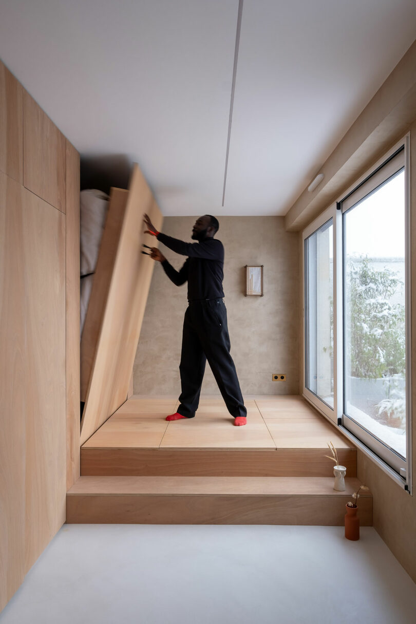 A person lifting a foldaway bed that is seamlessly integrated into the wooden platform.