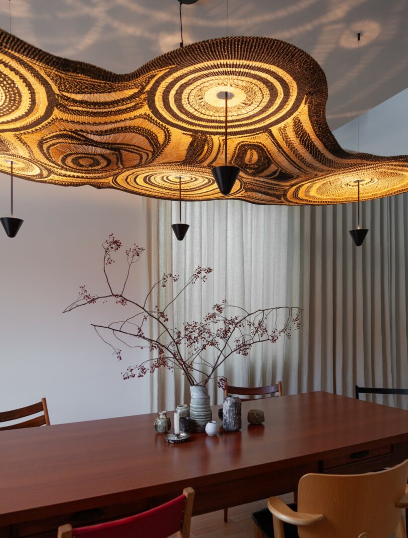 A minimalist dining room with a large sculptural woven pendant light hanging above a wooden dining table.