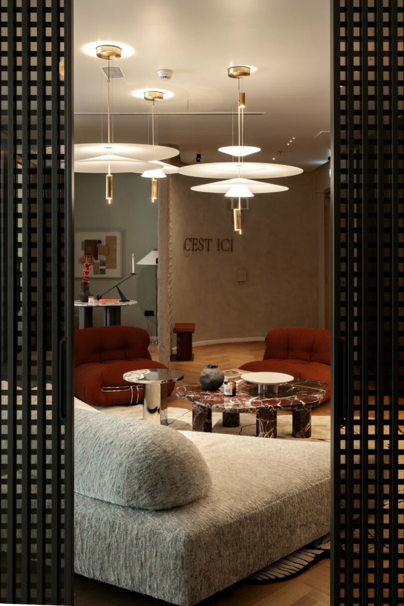 Modern lounge area at C’est ici Design with red chairs, a gray sofa, and marble accents.