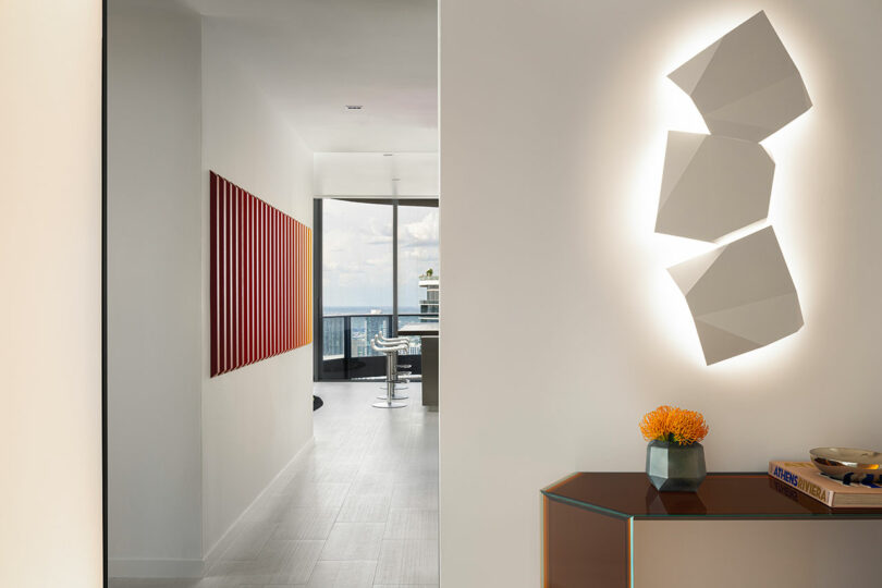 Modern hallway featuring geometric wall lighting and a large piece of red abstract art on the wall.