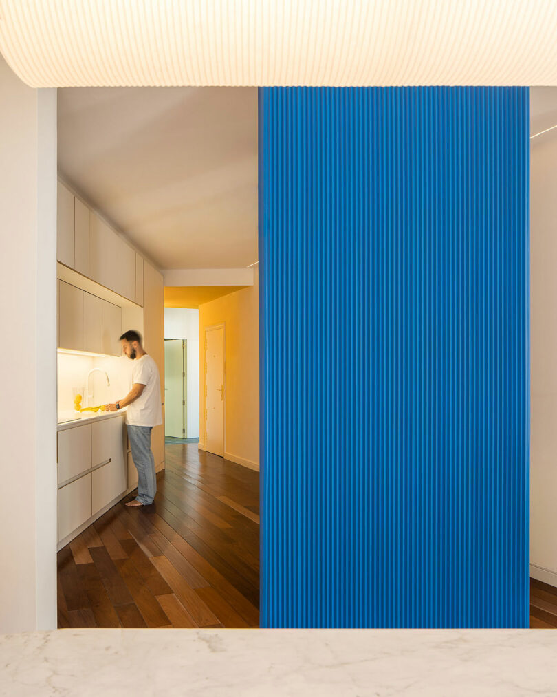 Close-up of a blue ribbed divider next to a person in a white kitchen with dark wood flooring.