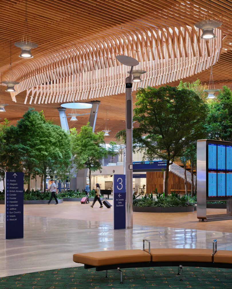 The interior of PDX terminal featuring the wooden lattice ceiling, indoor trees, and a digital flight board.