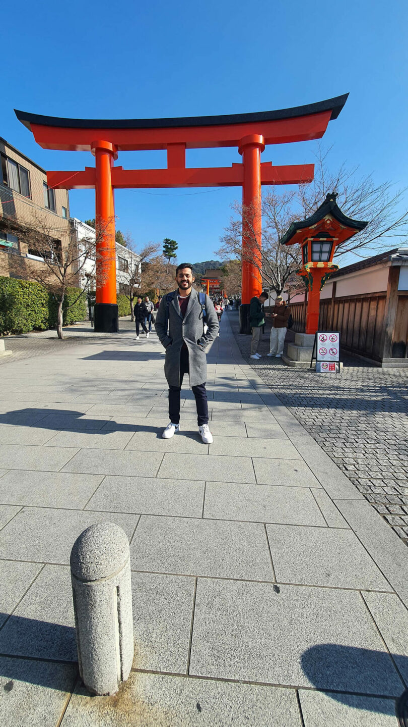 A traditional Japanese red Torii gate with a person standing in front of it.