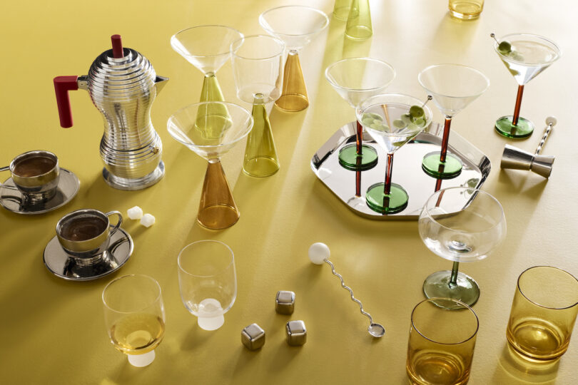 Vibrant cocktail accessories and hand-blown glassware arranged on a bright yellow surface.
