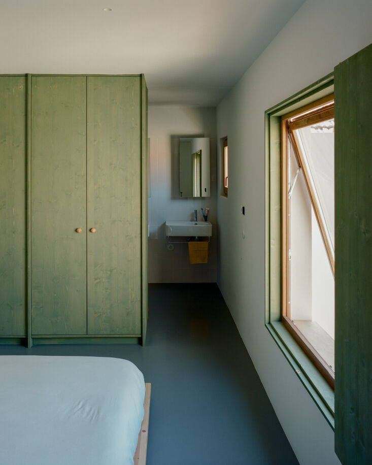 A minimalist bedroom featuring wooden closets and a large window overlooking the courtyard.