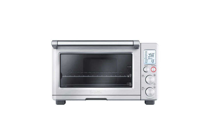 A compact stainless steel Breville smart oven sitting on a wooden shelf.