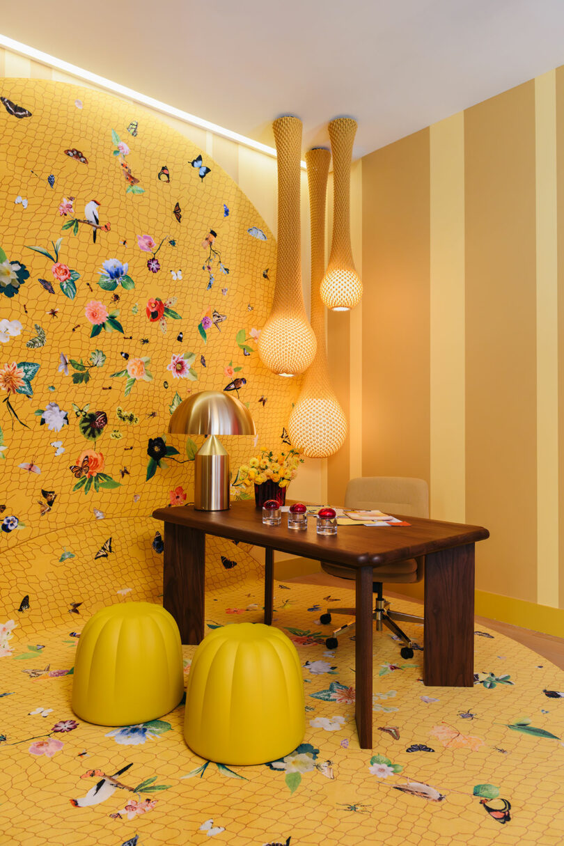 Modern office workspace within the gallery featuring yellow stools, floral wall patterns, and warm lighting.