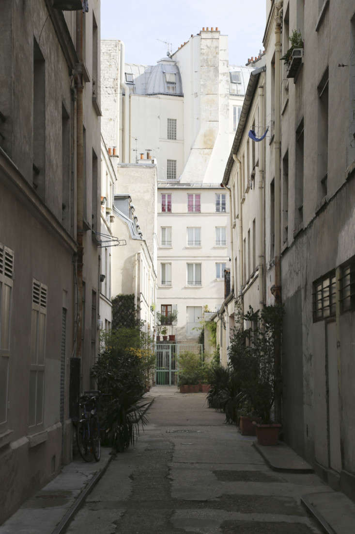 Exterior view of a 1960s industrial warehouse tucked behind traditional Parisian apartment buildings.