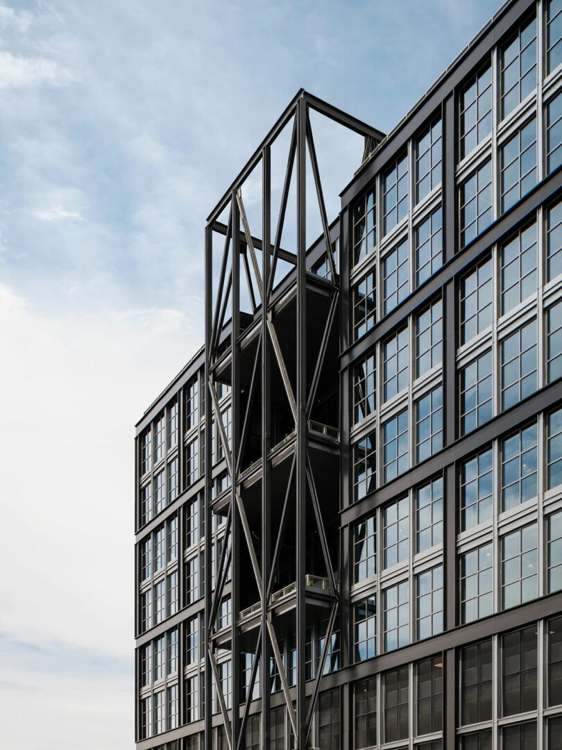 A close-up of the Steel House facade featuring prominent diagonal black steel beams against glass panels.
