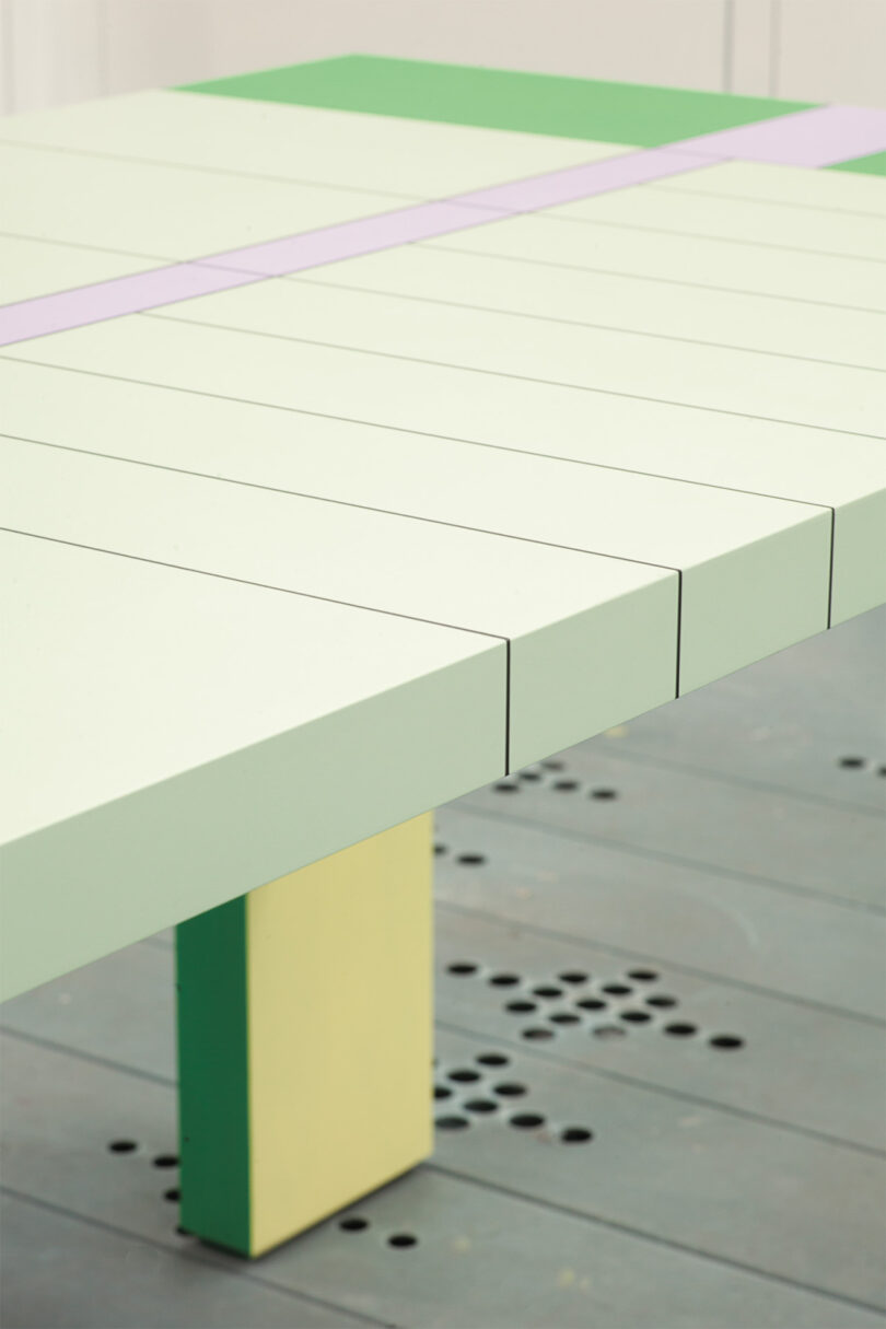 Close-up of a modern table surface featuring light green grooves, a lilac stripe, and a yellow leg.