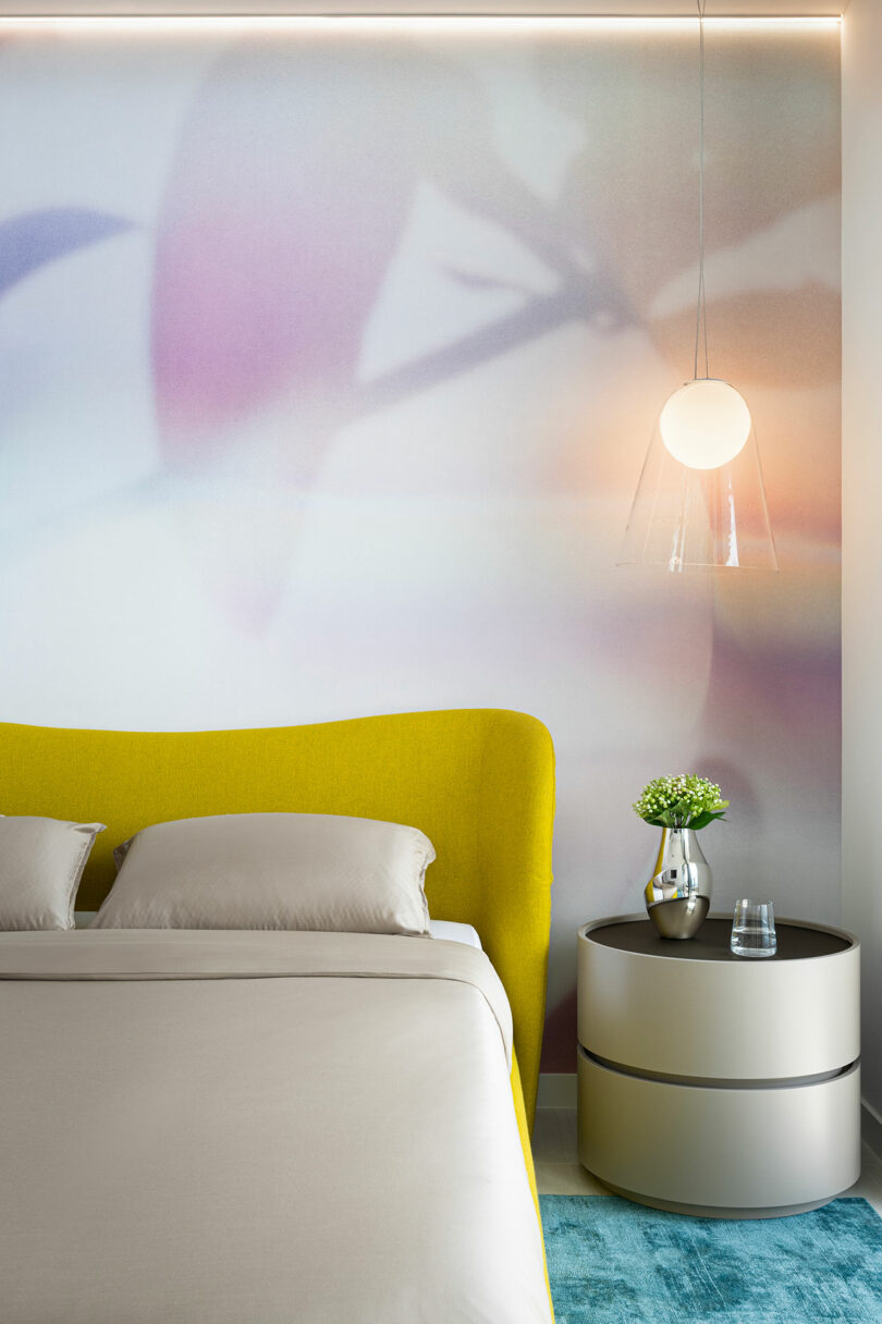 Modern bedroom featuring a soft pastel wall mural, a yellow headboard, and a spherical pendant light.