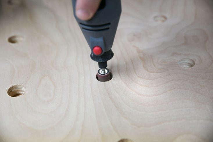 Hand sanding the interior of a circular hole in the plywood pegboard.