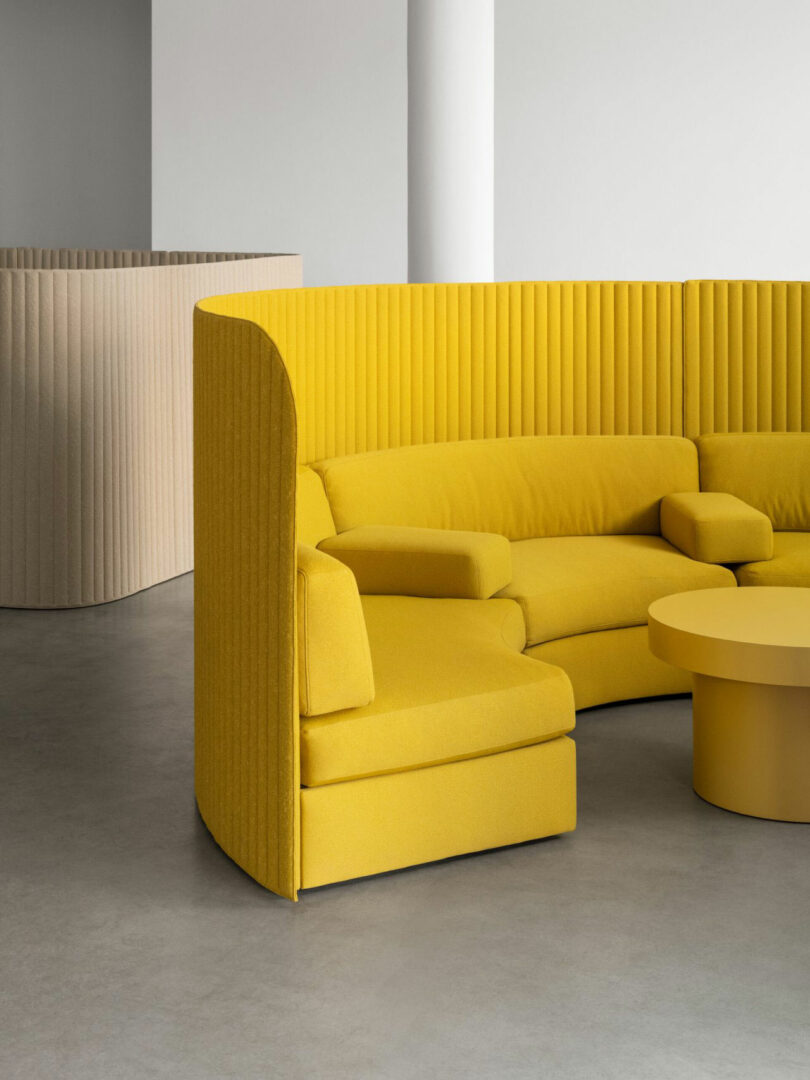 A curved yellow sectional sofa with a high ribbed backrest and a matching round table.