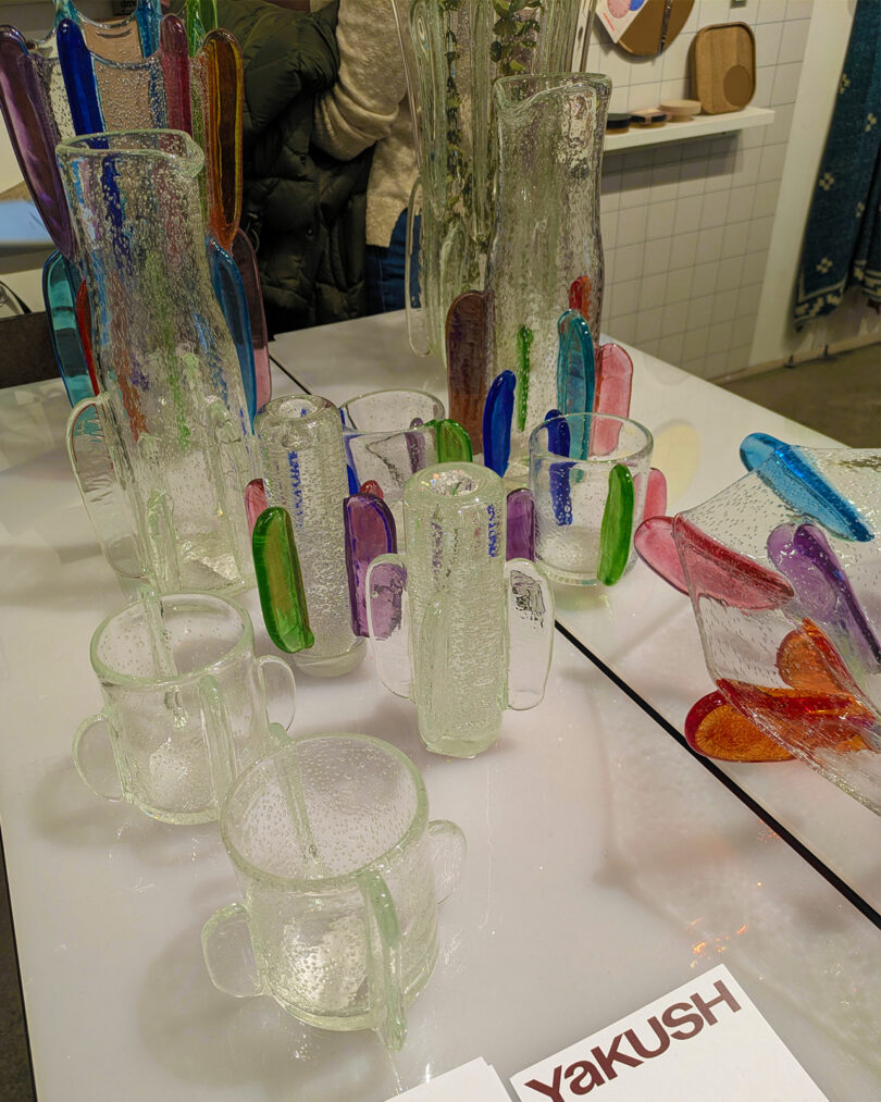 Clear glass pitchers and mugs with vibrant, colorful handles on a display table.