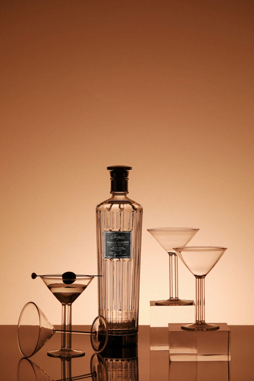 A Chopin Family Reserve Vodka bottle next to two empty and one filled Ernestine martini glass.