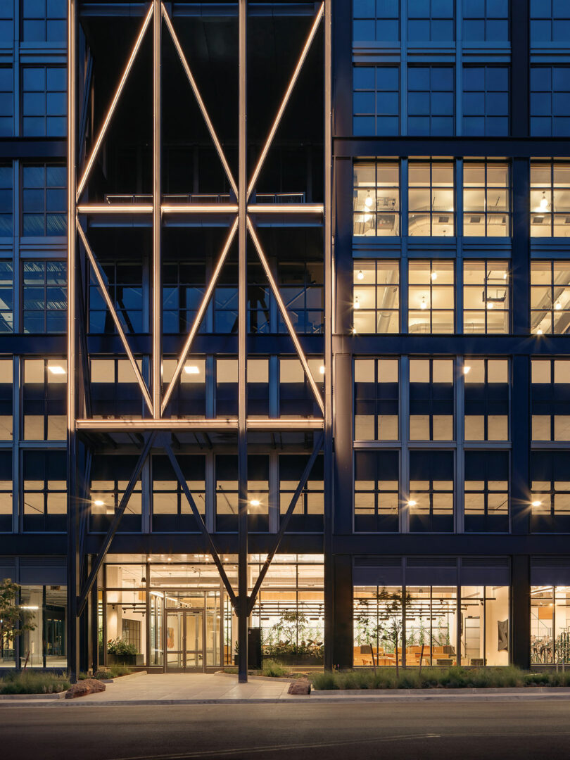 The facade of Steel House at dusk, with geometric lights glowing through the glass windows.