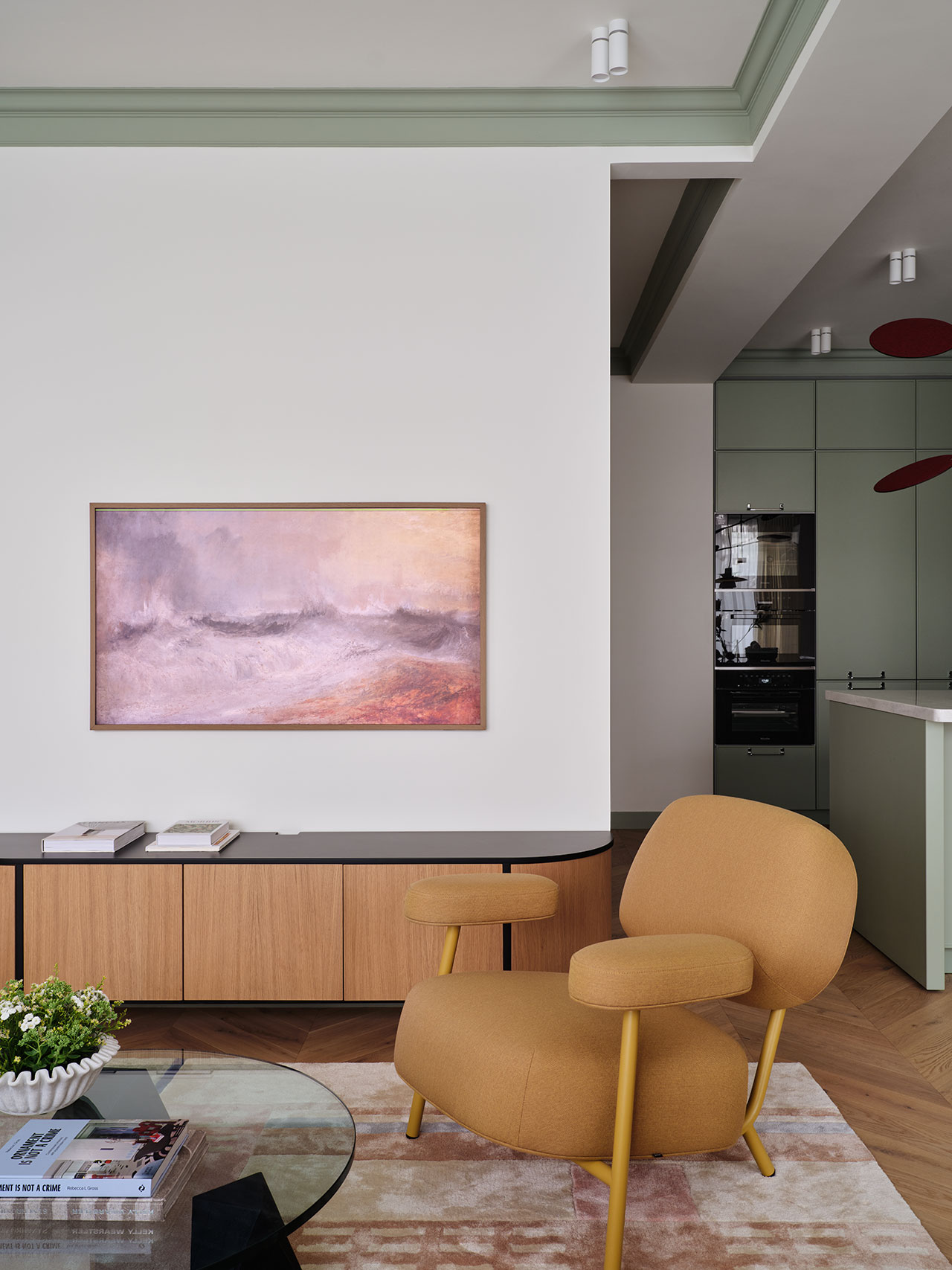View from a modern living room featuring a mustard armchair looking into a sage green kitchen.